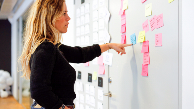 Bild på kvinna som står framför en skärm med ett antal postit-lappar