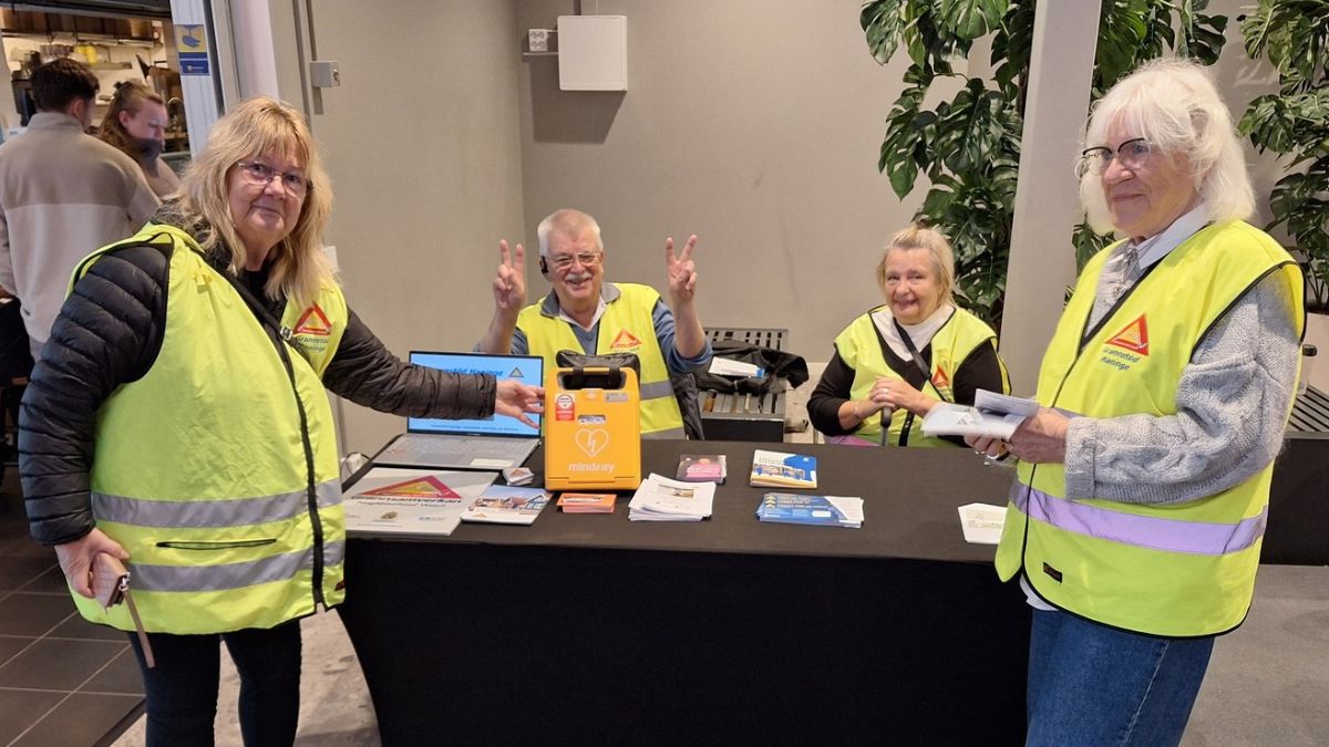Fyra personer från Grannstöd Haninge står vid ett informationsbord. På bordet står en hjärtstartare som har köpts in med hjälp av prispengarna från Haninge kommuns trygghetspris 2025.