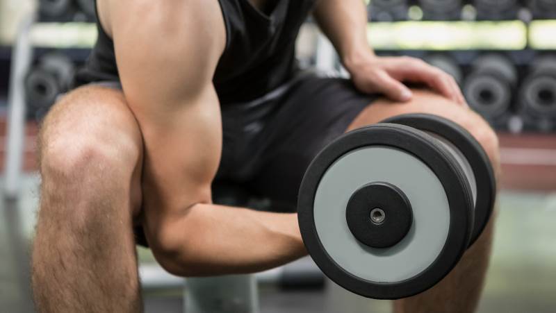 Man sitter på bänk i gym och lyfter en hantel