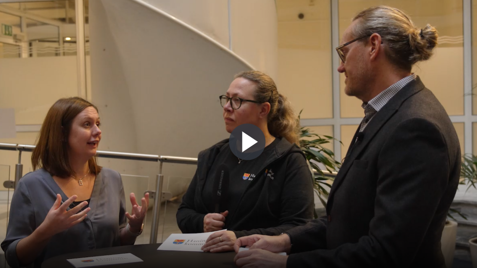 Tre personer ståendes runt ett bord och samtalar. 