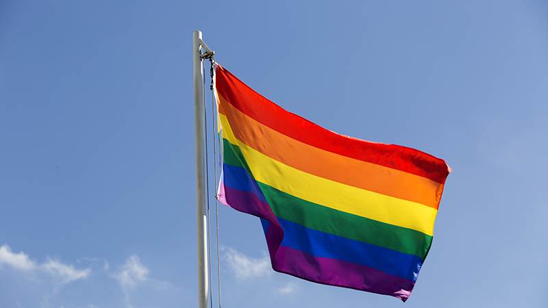 Regnbågsflagga på flaggstång mot blå himmel
