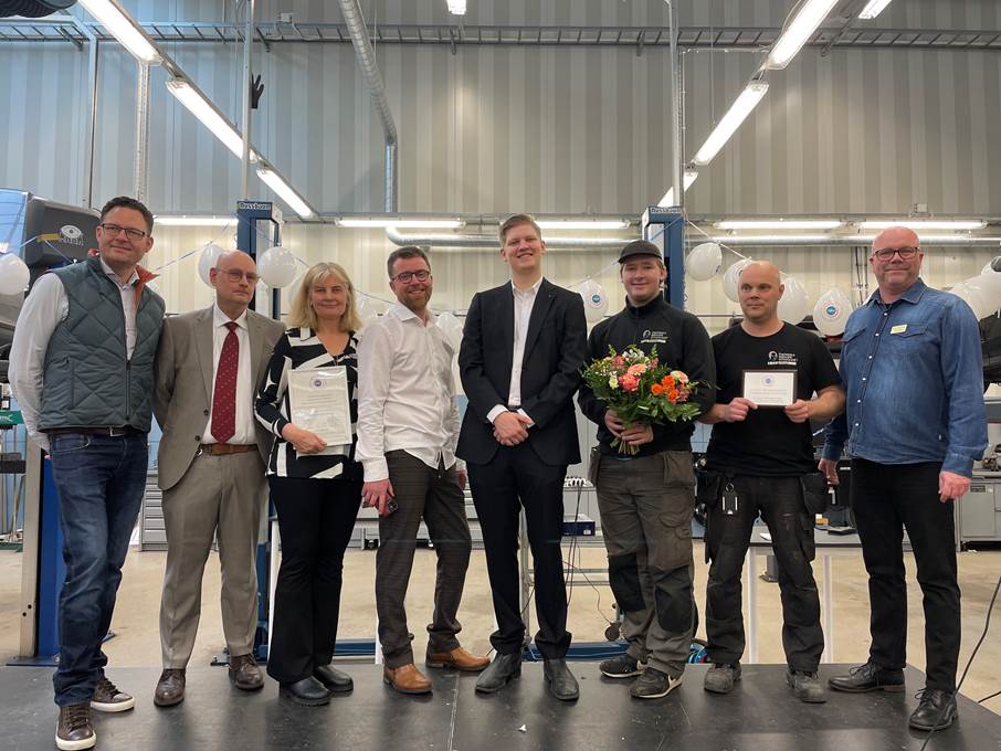 Sju män och en kvinna i en motorhall på Fredrika Bremers gymnasium med certifieringar och buketter
