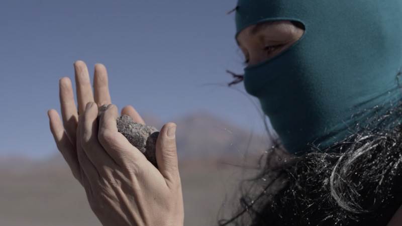 En maskerad kvinna håller stenar i händerna