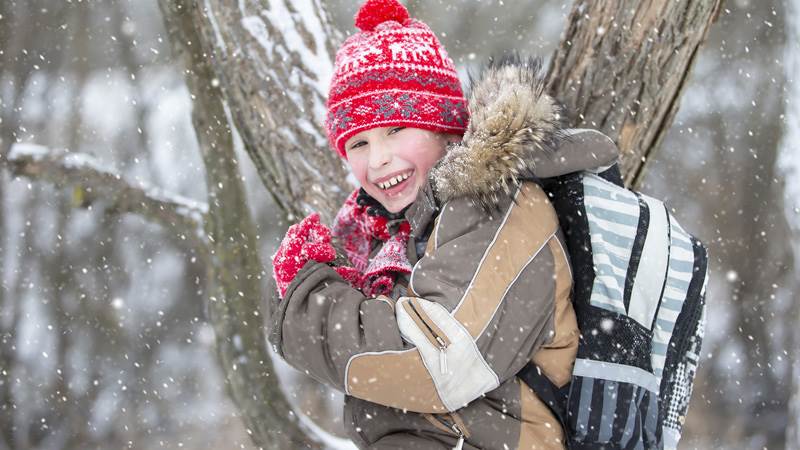 Glad pojke ler mot kameran medan snö faller