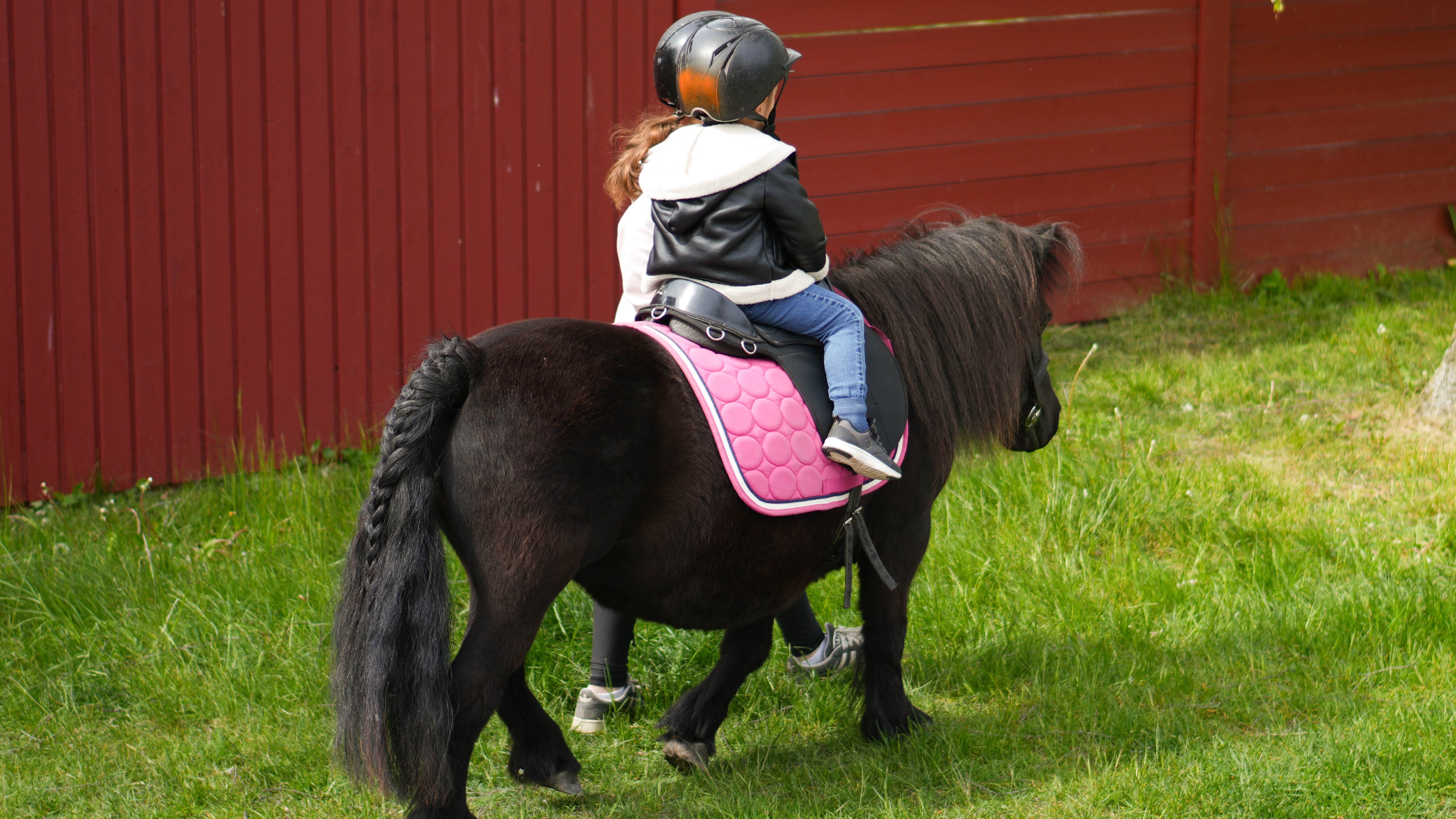 Barn som sitter på en ponny och som leds av en tonåring