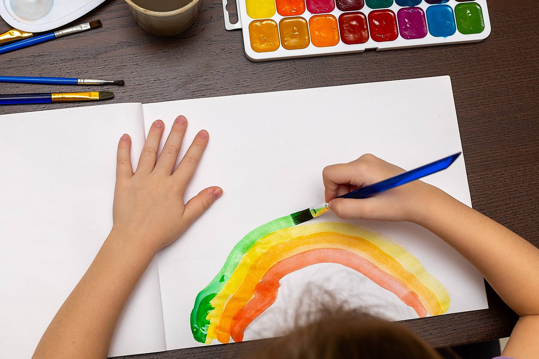 Ett barns händer som målar en regnbåge med starka, färgglada färger.