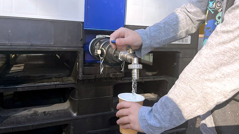 Ett barn tappar upp vatten från en kran utomhus