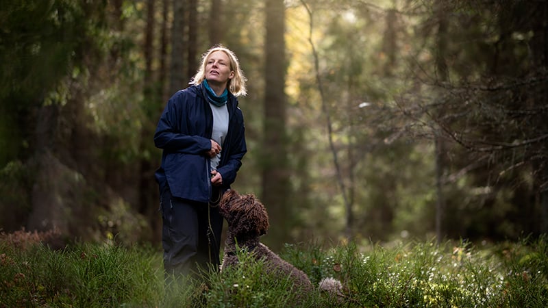 Kvinna i skogen med hund i koppel