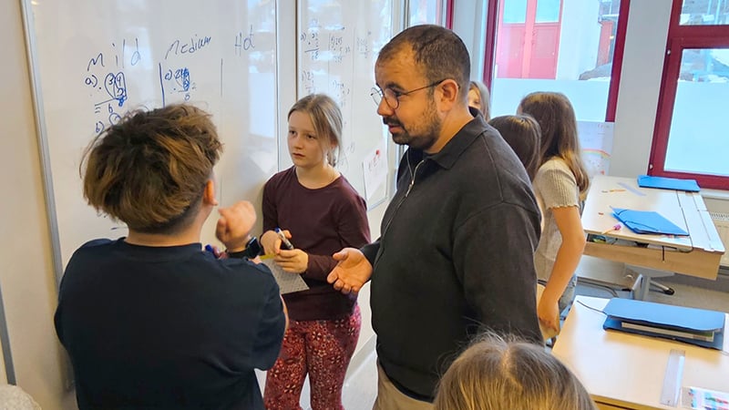 En lärare hjälper elever vid en whiteboard.