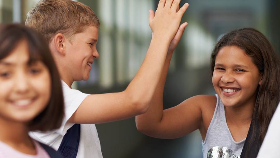 Två tonåringar ser glada ut och gör high five.