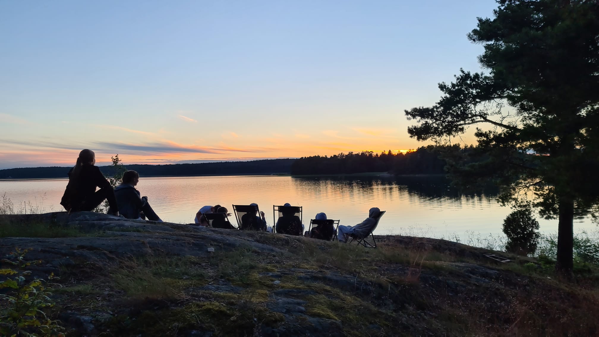 Ungdomar på en klippa i solnedgång.