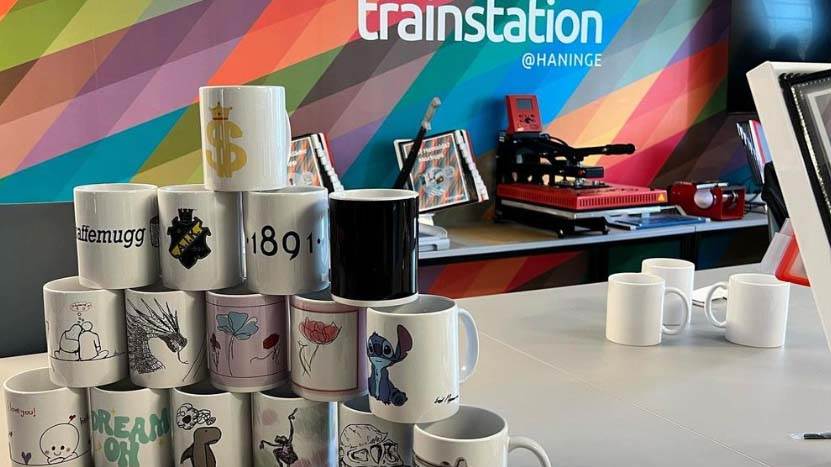 Muggar med olika tryck framför Trainstations logga.