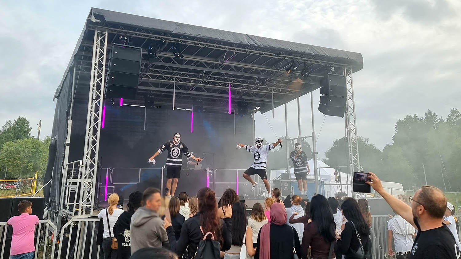 Ungdomar framför en scen där maskerade män uppträder.