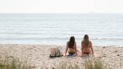 Två tjejer sitter på stranden och kollar ut över havet