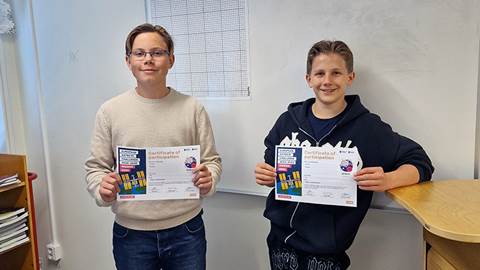 Två pojkar står i ett klassrum och håller upp varsitt diplom.