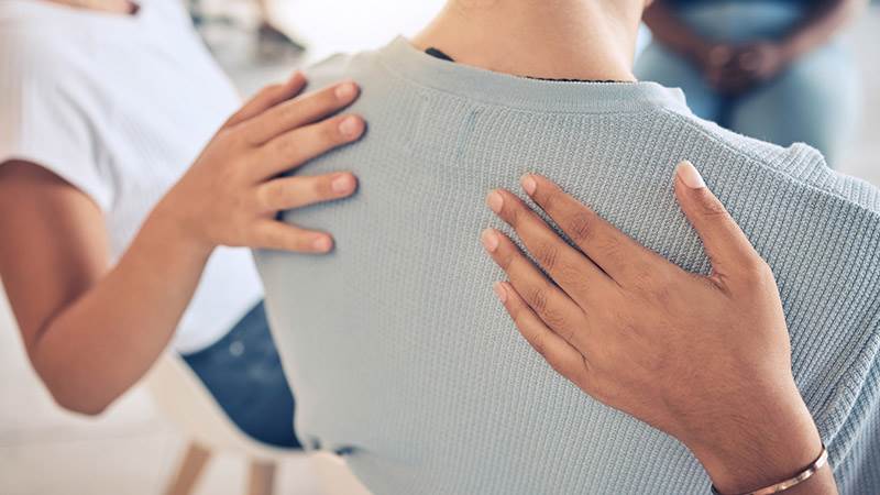 En person sitter på en stol och två andra personer håller hen om ryggen