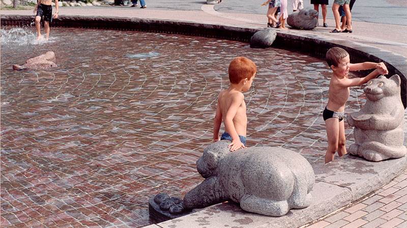 Två barn leker i plaskdammen med stenstatyerna En fågel i handen