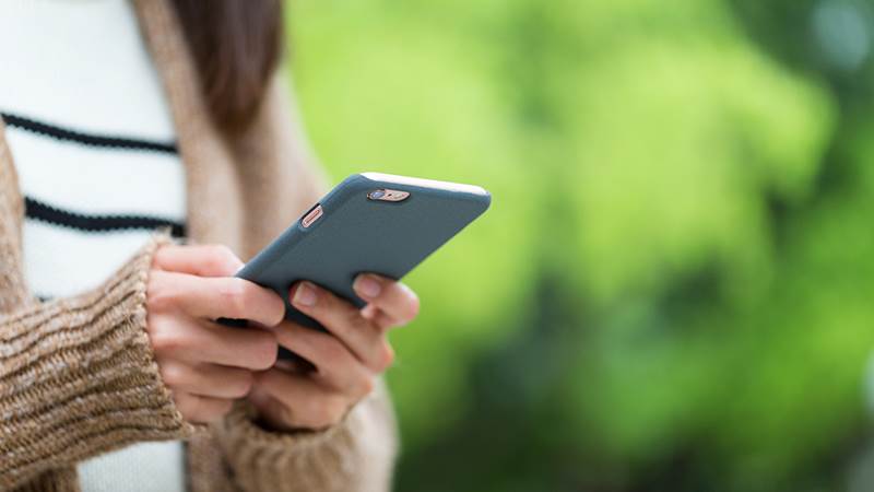 Kvinna utomhus med en mobiltelefon i sina händer.