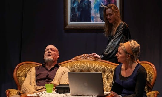 En man och två kvinnor i en soffa på en  teaterscen