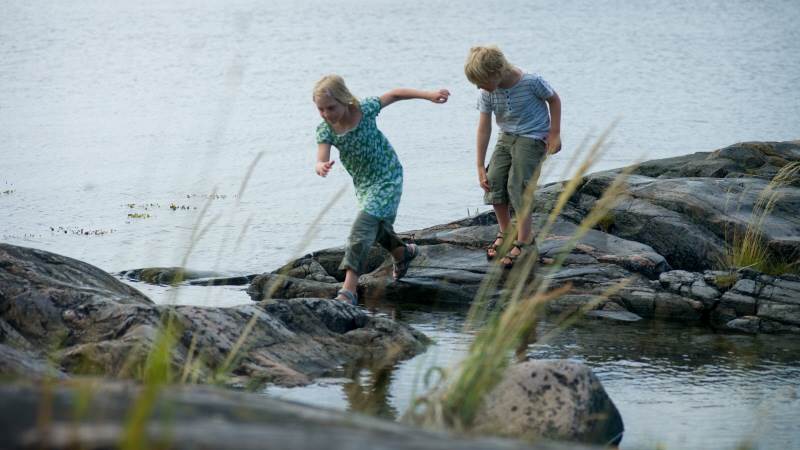 En flicka och en pojke balanserar på stenar på vattnet.