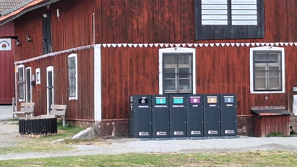 Insamlingskärl står på rad mot en röd husvägg