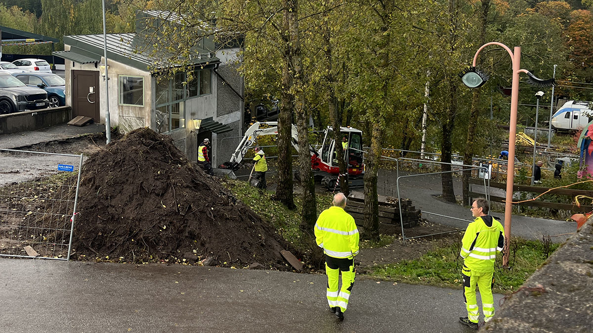 En grävmaskin som grävt upp jord och arbetare klädda i neongula kläder.