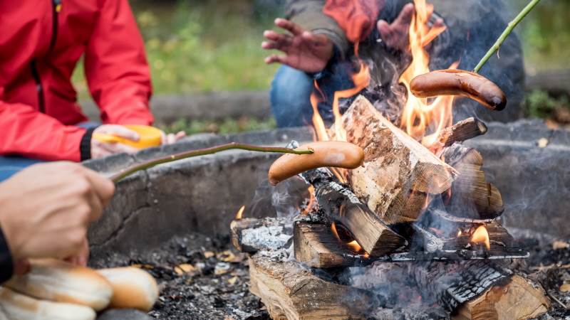 Eld som brinner och händer som grillar korv på pinne och galler.