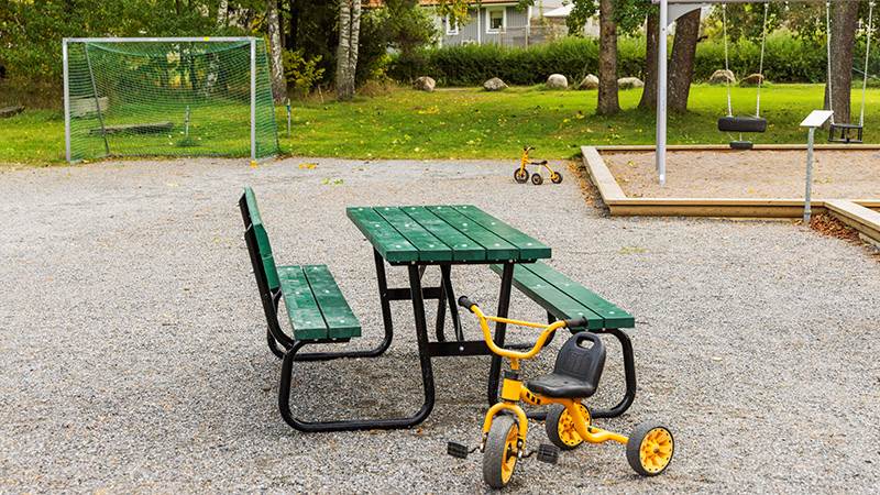 Grönt bord med sittplatser och en gul trehjuling på en lekplats