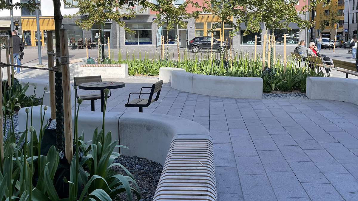 Stenlagt torg med slingrande sittplatser och grönska