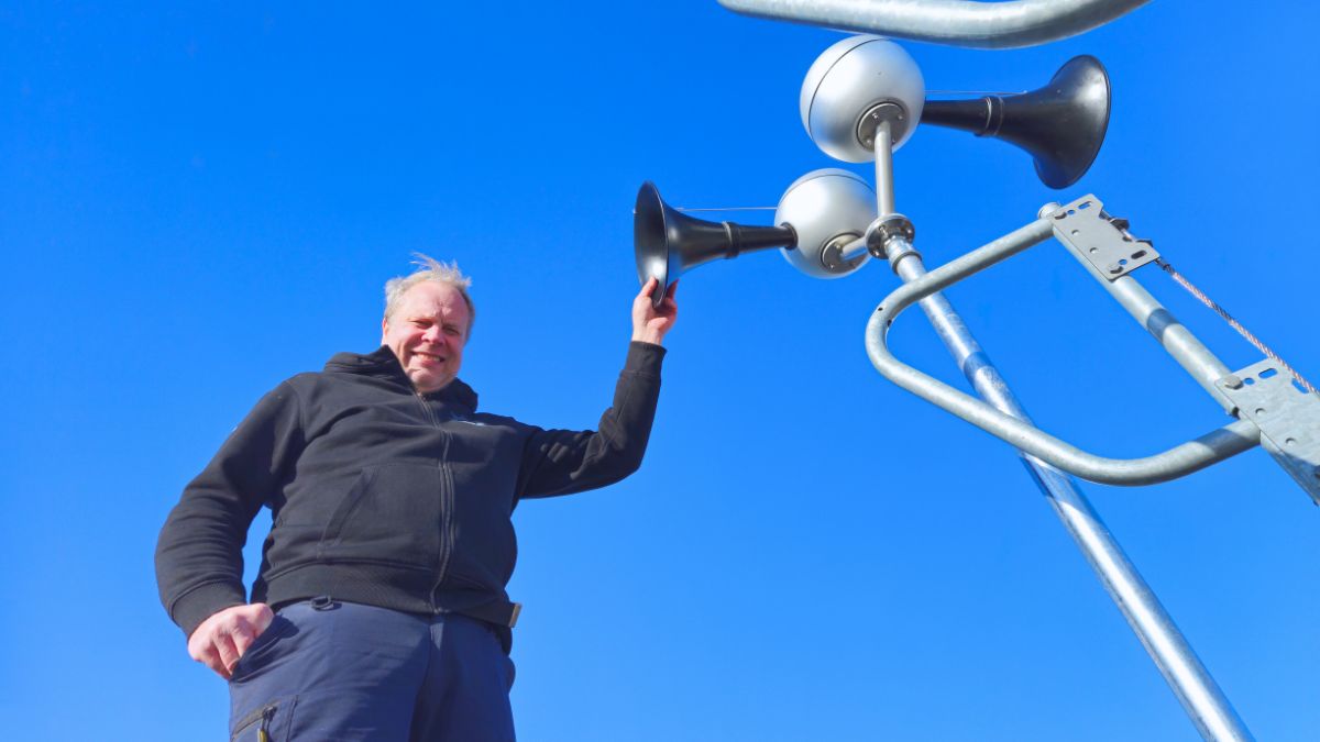 Installatör lyfter arm mot tydon på stolpe under montering mot klar blå himmel.