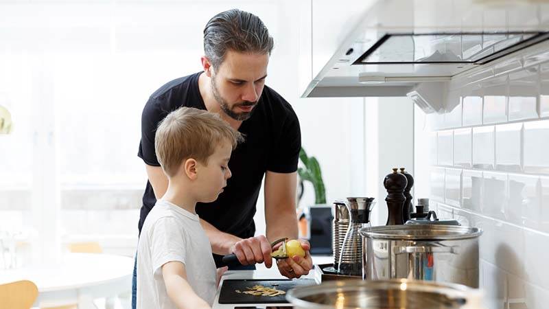 En vuxen man och ett barn skalar potatis tillsammans