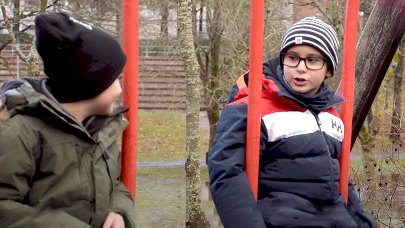 Två pojkar sitter och pratar med varandra på varsin gunga