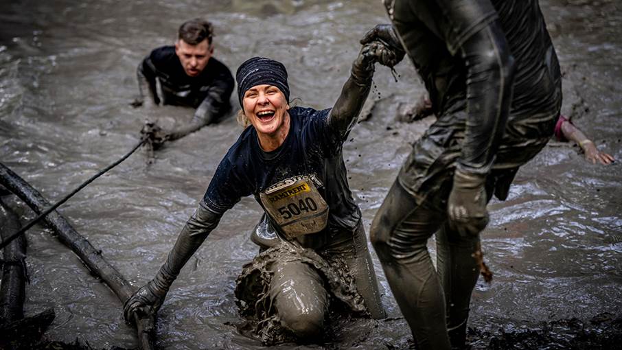 Glad kvinna klättrar upp ur en lerig pöl.