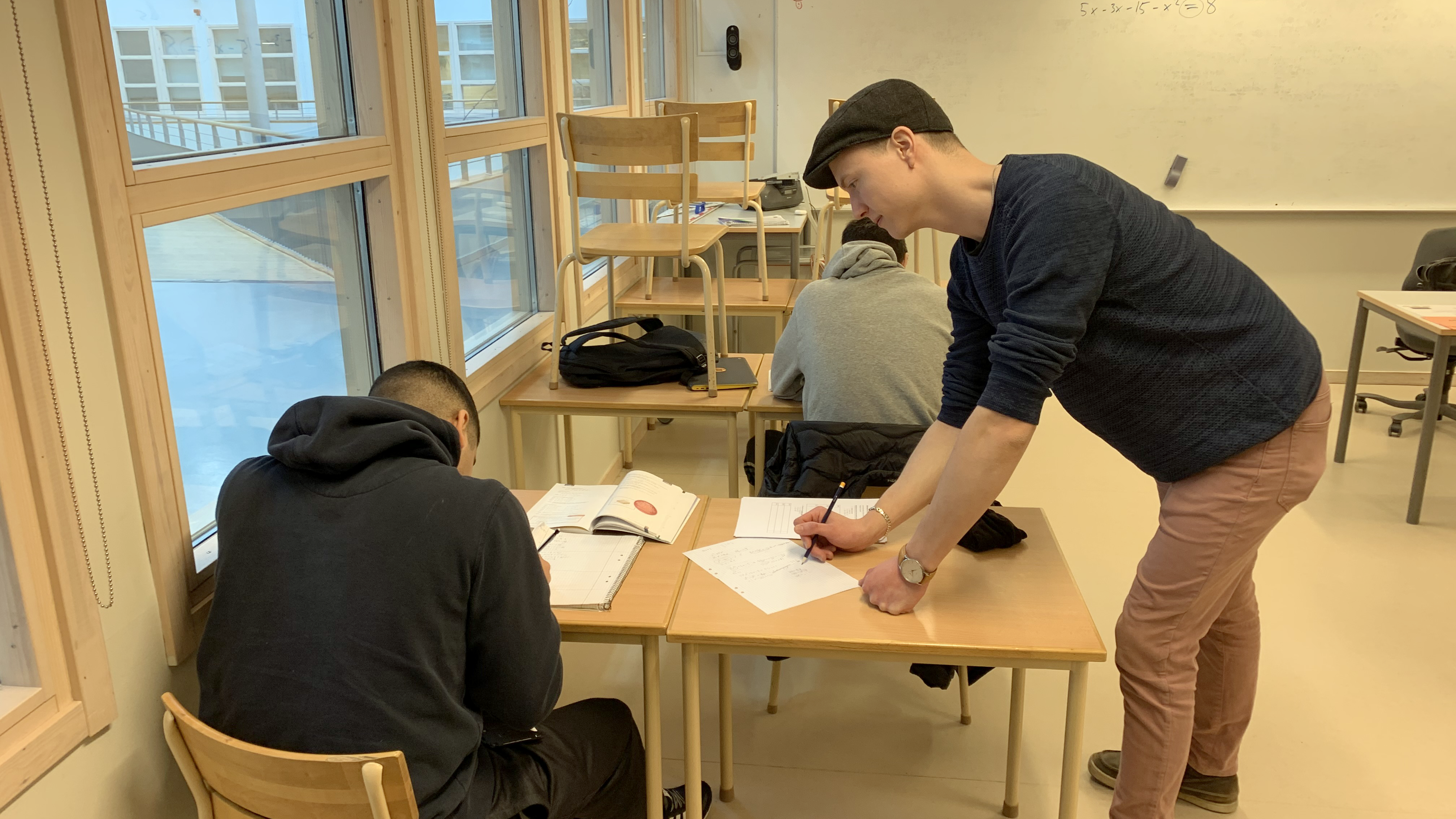 En lärarstudent står lutad över en elev och hans arbete, lärarstudenten hjälper till under en lördagsskolelektion.