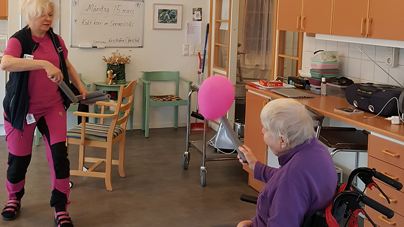 Personal och en äldre person i rullstol spelar ballongtennis.