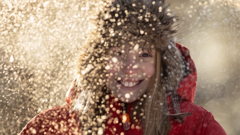 Flicka som ler glatt mot kameran med snö som faller framför henne
