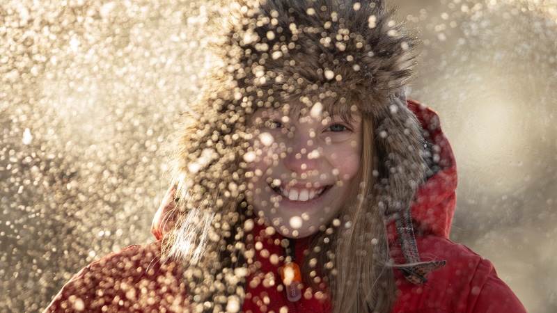 Flicka som ler glatt mot kameran med snö som faller framför henne