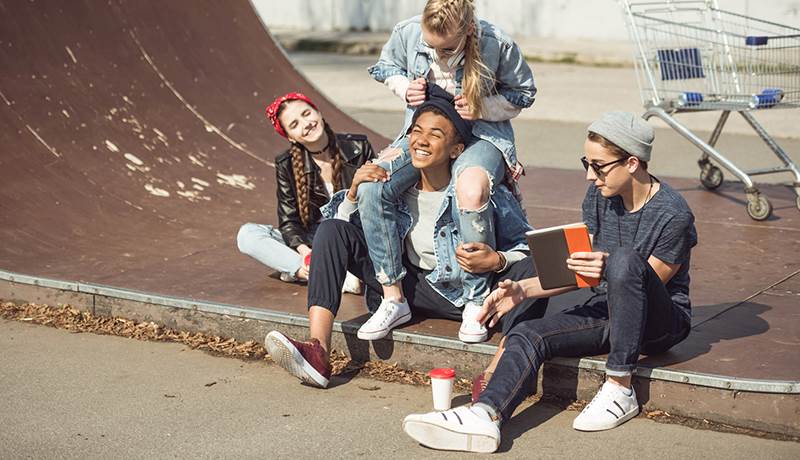 Ungdomar sitter utomhus i skateramp och skrattar.