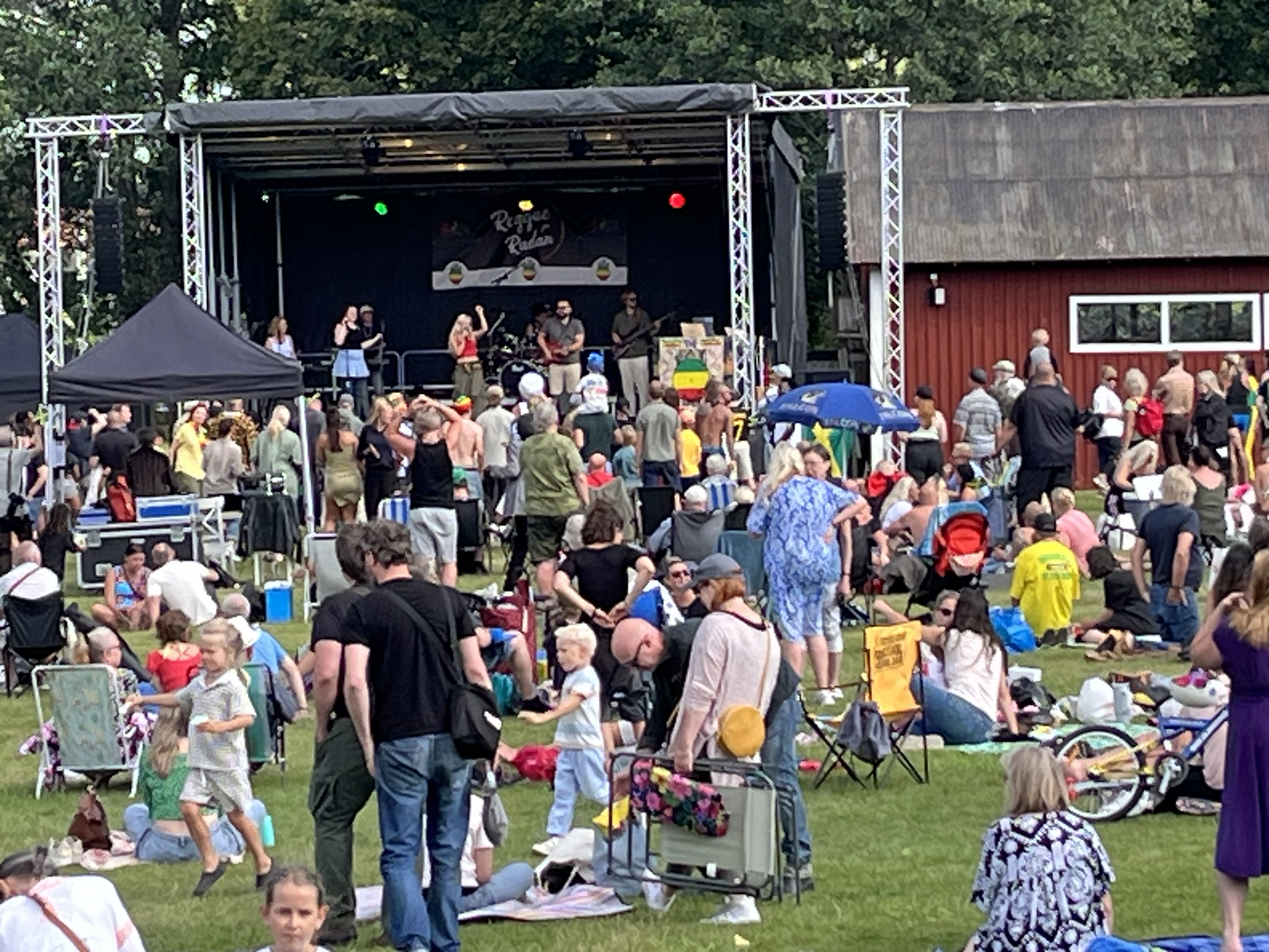 Massor av människor ståendes och sittandes på en gräsmatta framför en scen där ett band uppträder.