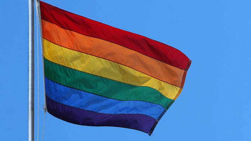 En Pride-flagga vajar i vinden med blå himmel i bakgrunden