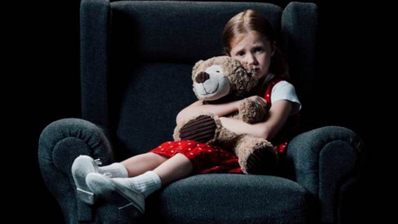 En flicka sitter i en fåtölj och kramar om en nalle