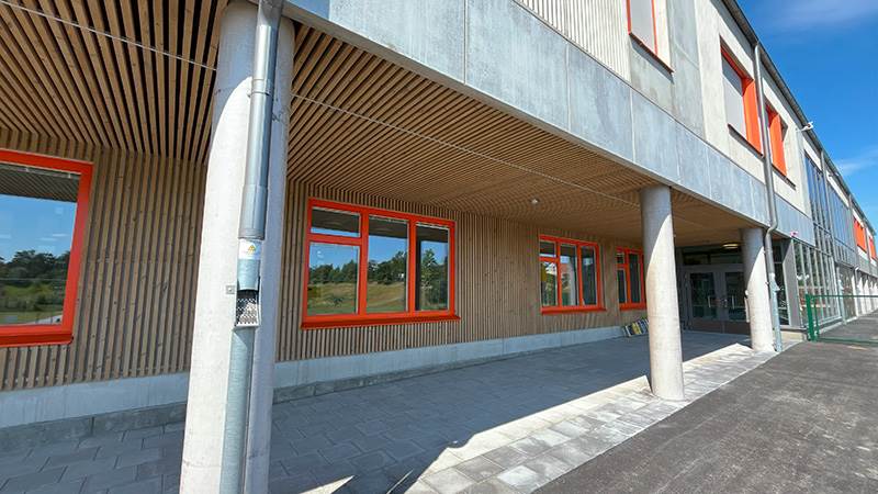 Entré till de praktiska och estetiska klassrummen samt till fritidsgården. Stort hus i trä och betong och orangea fönsterkarmar