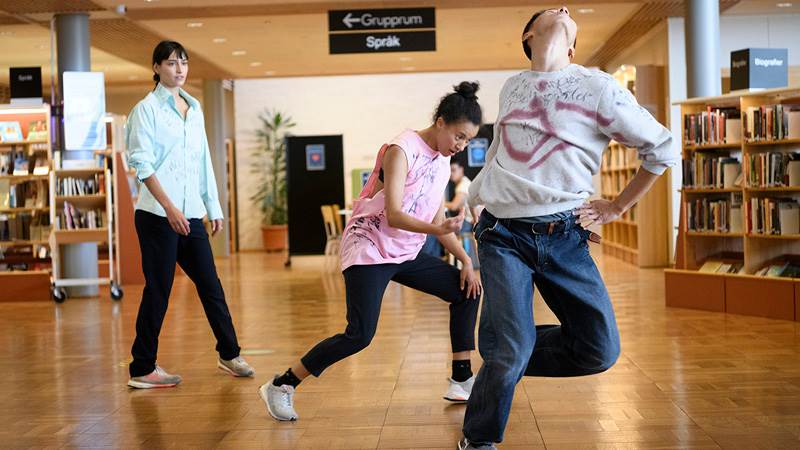Tre personer dansar i ett bibliotek