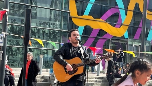 En person står på ett torg och sjunger i en mikrofon samtidigt som personen spelar gitarr.
