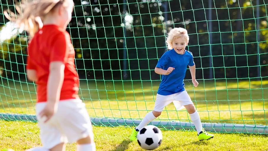 Två barn spelar fotboll utomhus.