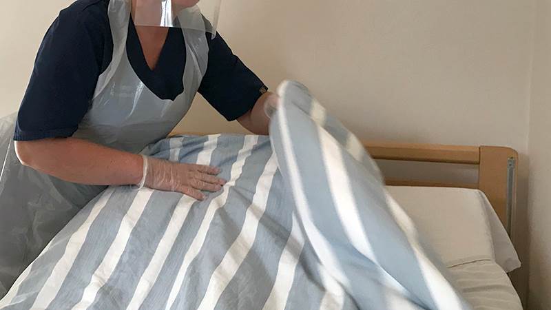 Person med förkläde och skyddshandskar bäddar en säng