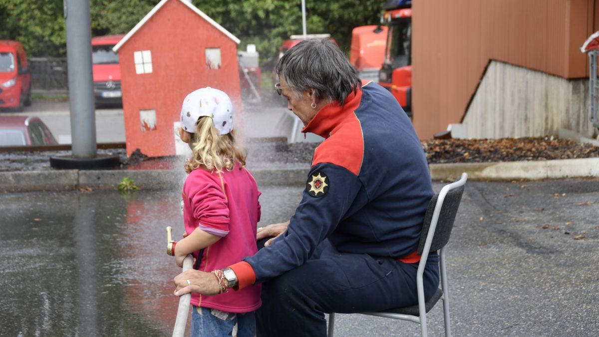 Ett barn provar att hantera en brandslang med stöd av en medarbetare under öppet hus på brandstationen.