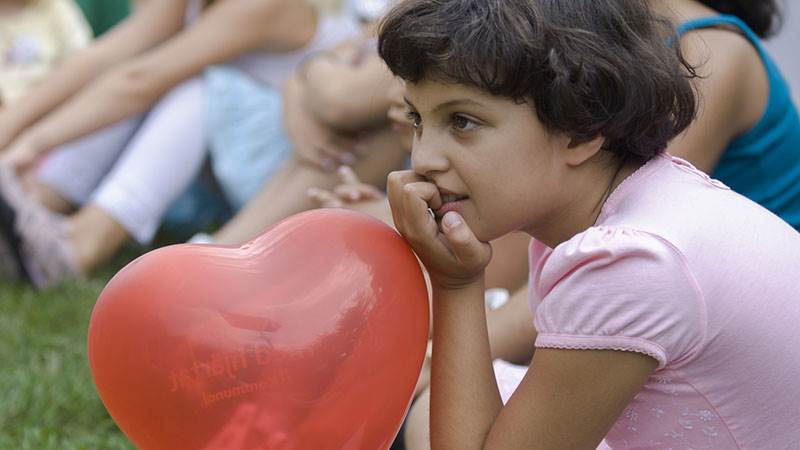 En flicka sitter på gräset med en röd ballong i form av ett hjärta