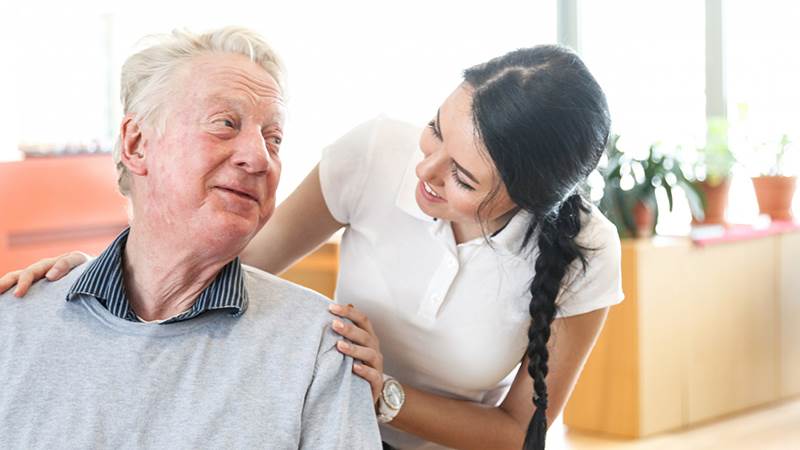 En äldre man och en sköterska ler mot varandra