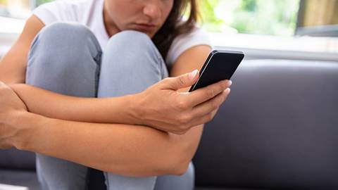 En kvinna sitter i en soffa och håller i en telefon